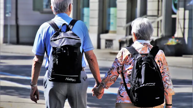 Älteres Paar mit Rucksäcken geht Hand in Hand durch die Stadt