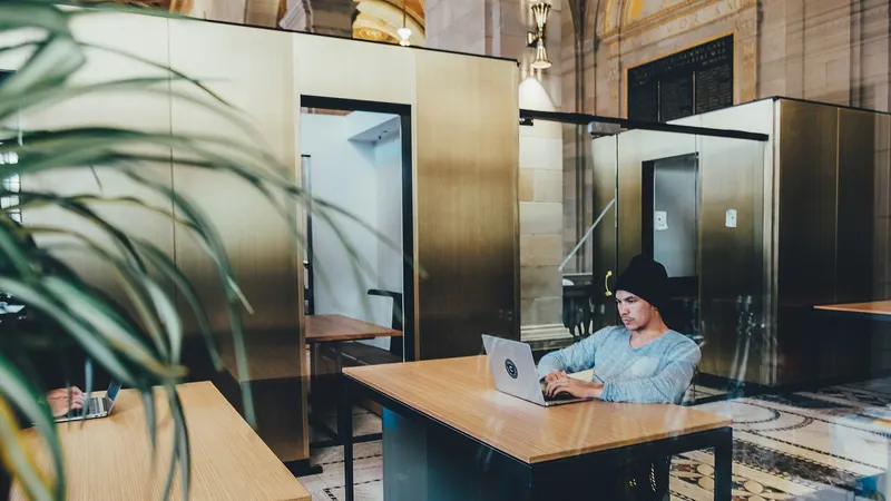 Salarié travaillant sur un ordinateur portable dans un espace de bureaux partagé, avec une plante au premier plan