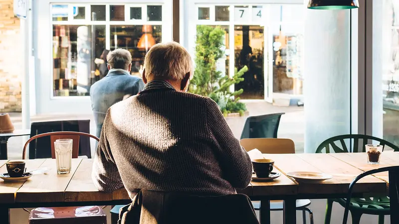 Homme âgé assis de dos à une table de café, devant une tasse