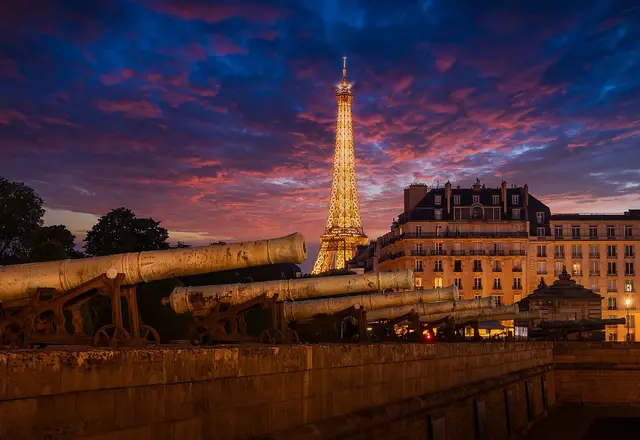 La tour Eiffel illuminée au crépuscule, avec d'anciens canons au premier plan